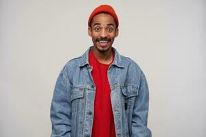 Studio photo of joyful young bearded dark skinned brunette guy in casual clothes raising surprisedly eyebrows while looking at camera with wide eyes and mouth opened, isolated over white background