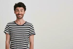 Closeup of happy handsome young man with bristle wears striped t shirt feels surprised and looks excited standing over white wall with copyspace for your advertising photo