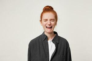 Upset red-haired girl with a bun on her head crying with closed eyes. A woman was upset, did not keep emotions and started to cry,depicts a sob photo