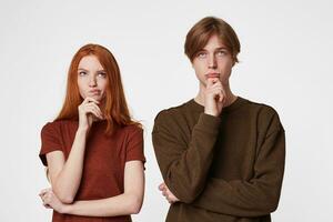 Focused concentrated young couple keep arm on chin and look thoughtfully up, being confused and questioned, thinking what to do to solve the problem, troubled, over white background photo