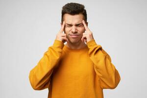 Young man focused eyes squeezed forefingers near temples trying to remember something, deep analysis of the situation, immersed in thoughts, dressed casually, isolated over white background photo