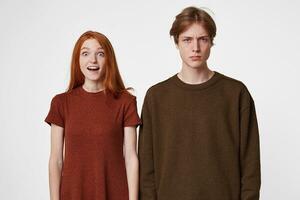 Boy and girl pose, depict different emotions. The red-haired girl is surprised, happy, delighted with a gift or a meeting. The guy next to her is sullen and unhappy. photo