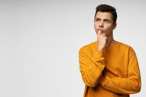 Waiting for inspiration. Thoughtful young man holding hand on chin and looking away standing isolated over white background. Copy space for advertisement photo