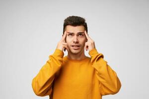 Young man ponders the idea, focused, looks up to the distance, forefingers near temples, trying to remember something, immersed in thoughts, dressed casually, isolated over white background photo