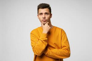 Handsome attractive young man ponders over a gift for a girl for a new year or birthday, remembers the latest events, thinking of something important holding his chin, looks into the distance photo