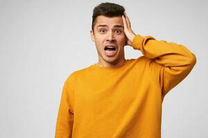 Headshot of irresponsible guy screaming because of catastrophe had happened. Frightened man holding his head, mouth opened, dressed casually, isolated over white background photo