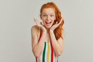 Happy looking woman, positive redhead girl with pony tail and freckles. Wearing striped colorful swimsuit. Shows amazement. Broadly smiling. Watching at the camera isolated over grey background photo