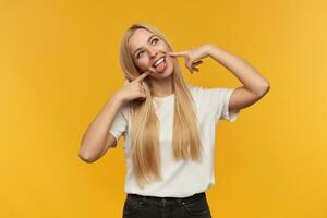 Adolescente chica, contento gracioso mirando mujer con rubio largo cabello. vistiendo blanco camiseta y negro vaqueros. personas y emoción concepto. acecho a el cámara, aislado terminado naranja antecedentes foto