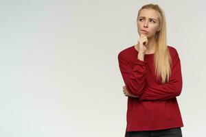 Portrait of attractive, adult girl with blond long hair. Wearing red sweater. People and emotion concept. Watching up thoughtfully at copy space, isolated over white background photo