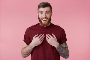 Close up of happy excited bearded man with tattooed hand, pointing at himself, looking at camera isolated over pink background. People and emotion concept. photo