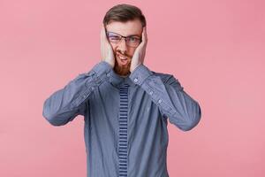 Portrait of young bearded busines man in glasses, tired of working, hard to think, confused, hold his head, isolated over pink background. photo