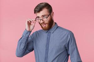 foto de un joven atractivo barbado hombre, mirando con desaprobación mediante su anteojos, colega hecho un estúpido Error en trabajar. aislado terminado rosado antecedentes.