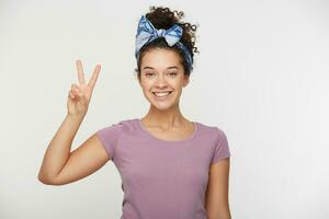 Portrait of a smiling happy woman showing victory sign and looking at camera isolated on the white background. Charming attractive girl showing v-sign gesture. photo