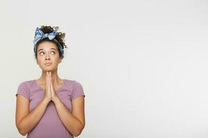 Portrait of young beautiful brunette girl praying, hands folded in prayer concept for faith, spirituality. Looking away. Copy space for you advertisement or promotional text, over white background photo