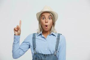 Portrait of inspired delighted surprised depicting wow facial expression young blonde, pointing index finger up to empty copy space, isolated on white background. photo