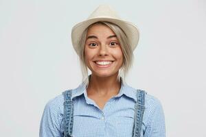 niña rubia en un blanco sombrero mira alegremente satisfecho feliz, sonrisas en general, un sobreabundancia de positivo emociones, felizmente suficiente, aislado terminado blanco antecedentes foto