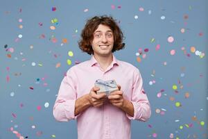 Close up of the birthday man takes photos with a gift box, holds it in his hands, looks camera, on his face an expression of bewilderment confusion, did not expect to receive such a small gift