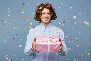 Close up of a man who gives a gift in a pink box with white ribbon, is going to give a modest gift from the heart, looking at the camera, confetti falling down. People, joy, fun and happiness concept. photo