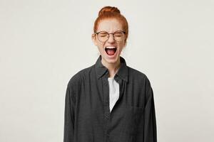 Close up of scared red-haired girl, feels frightened afraid, mouth wide opened as screaming shouting yelling loud, eyes closed, over white background photo