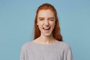 Cheerful lighthearted red-haired girl, winks at the camera, playfully looks, flirts, having fun, dabbling, with a positive mood isolated on a blue background. photo