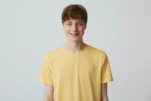 de cerca de contento hermoso joven hombre con corto Corte de pelo y tirantes en dientes usa amarillo t camisa en pie y sonriente aislado terminado blanco antecedentes foto