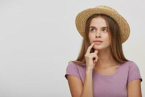 Teenage girl in a straw hat with a pink ribbon looks aside up puzzled, trying to remember something important, thoughtful, blank copy space on the left, place for advertisement, over white background. photo