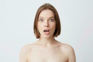 Horizontal shot of surprised pretty young woman with healthy soft skin after applying mask or body cream and opened mouth shouting and looks amazed isolated over white background photo