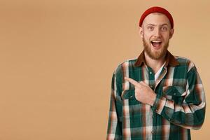Indoor shot of amazed excited man feels successful, pointing at left corner on blank copy space, dropping jaw standing rightside isolated over beige background, says omg or wow. photo