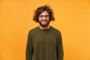 Cute friendly bearded man in glasses with curly hair smiling looks happy isolated on yellow background. A good friend came to visit, a niceguy. photo