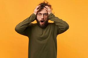 Oh my God, disaster, man in glasses opened mouth in panic, isolated on a yellow background. Guy clutched at his head in a panic, in despair, shocked. photo