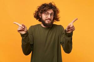 bearded guy in glasses pointing his index fingers on both sides,pretends that he has nothing to do with it, at a loss, experiencing suffering of choice making,isolated over yellow background photo