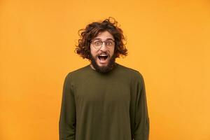 Shoot of a attractive man looks happy glad joyfully mouth widely open like heard a good news, see something great, wears casual longsleeve, on a yellow background in the studio. photo