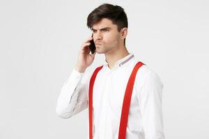 Portrait of a guy who talks on the phone feels angry irritation look turned to the side, on white background. Male client can not receive support from the call center manager can not solve his problem photo