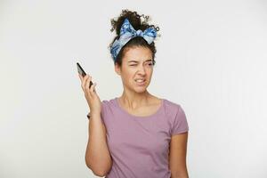 Portrait of girl keeps the phone at a distance from the head in hand, frowns at the fact that the other person shouts, swears, an unpleasant telephone conversation, a quarrel. Over white background photo