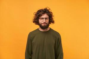 A bearded man in glasses with dark curly hair looking at the camera with a frustrated expression of his face, pursed his lips. Displeased with the result. Expecting more. photo