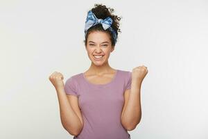 Enthusiastic motivated attractive young woman giving a fists up gesture of victory and success with a beaming smile, isolated over white background photo