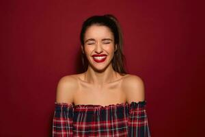 agradable mirando joven bonito largo peludo morena mujer con festivo maquillaje demostración su Perfecto blanco dientes mientras riendo felizmente, en pie terminado borgoña antecedentes foto