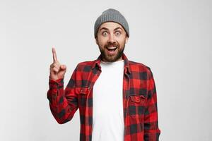 Great idea. Smiling young man keeping finger raised and looking at camera while standing against white background. Bearded cheerful man has fresh idea. Birth of ideas. photo