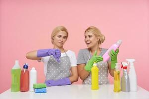 Indoor shot of young white-headed women with casual hairstyle dressed in uniform while posing over pink background, preparing for spring cleaning and choosing detergents photo
