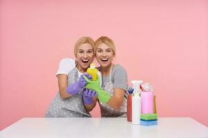 Excited young joyful white-headed twins laughing happily while looking at camera and hugging each other, being in high spirit while posing over pink background in working wear photo
