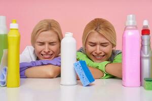 Indoor photo of sad young blonde housewives being exhausted after spring cleaning and frowning their faces while crying with closed eyes, posing over pink background