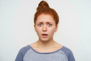 Frightened young redhead pretty woman frowning her eyebrows while looking confusedly at camera, keeping her hands down while posing over pink background photo
