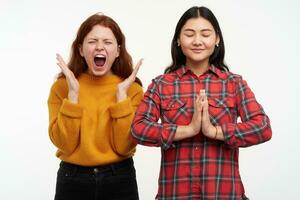 personas y estilo de vida concepto. niña carcajadas en ira mientras su amigo calma meditando, doblez manos en namaste signo. vistiendo amarillo suéter y a cuadros camisa. estar aislado terminado blanco antecedentes foto