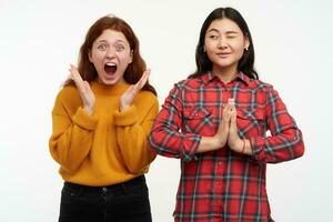Portrait of asian and caucasian friends. People and lifestyle concept. Girl trying to meditate while her friend screams. Wearing casual outfit. Watching at the camera, isolated over white background photo