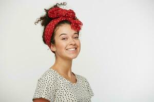 Shot of pretty satisfied female widely smiles, rejoices good offer, glad to participate in interesting event, stands sideways, dressed in T-shirt with black polka dots, isolated over white studio wall photo