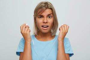 Portrait of confused beautiful blonde young woman with braces on teeth wears blue t shirt looks embarrassed and holding earphones isolated over white background photo