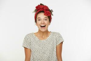 People and reaction concept. Happy overjoyed young woman reacts on positive news, has broad smile and surprised expression, wears T-shirt and red scarf with polka dots, poses against white background photo