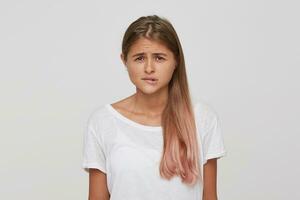 Closeup of sad upset young woman with long dyed pastel pink hair wears t shirt feels worried and biting her lip isolated over white background photo