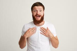 Portrait of happy surprised bearded young man with opened mouth wears t shirt looks, looks impressed and points at himself with both hands isolated over white background photo