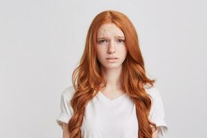 de cerca de Deprimido trastornado pelirrojo joven mujer con largo ondulado pelo usa t camisa siente desesperado y triste aislado terminado blanco antecedentes mira directamente en cámara foto